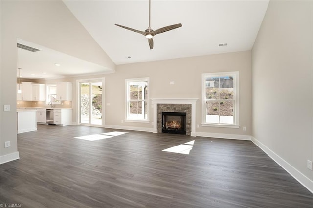 unfurnished living room featuring a tiled fireplace, ceiling fan, dark wood-type flooring, and a wealth of natural light