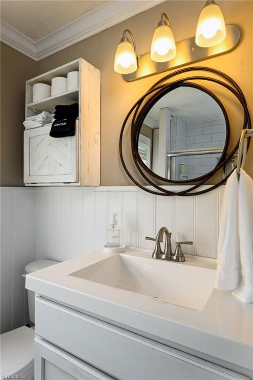 609 W Lexington Ave, High Point, NC 27262 - bathroom with vanity, ornamental molding, a decorative wall, and a wainscoted wall