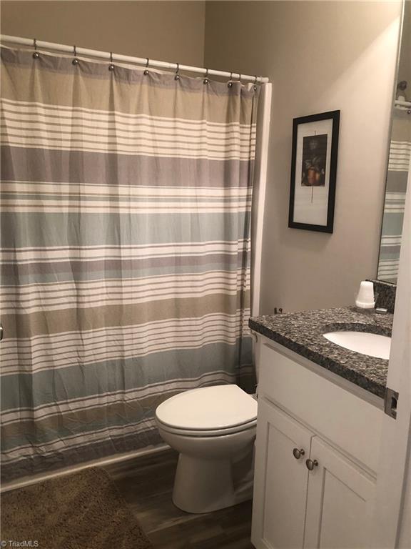 full bath with curtained shower, vanity, toilet, and wood finished floors