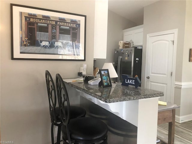 bar featuring baseboards, wood finished floors, and stainless steel fridge with ice dispenser