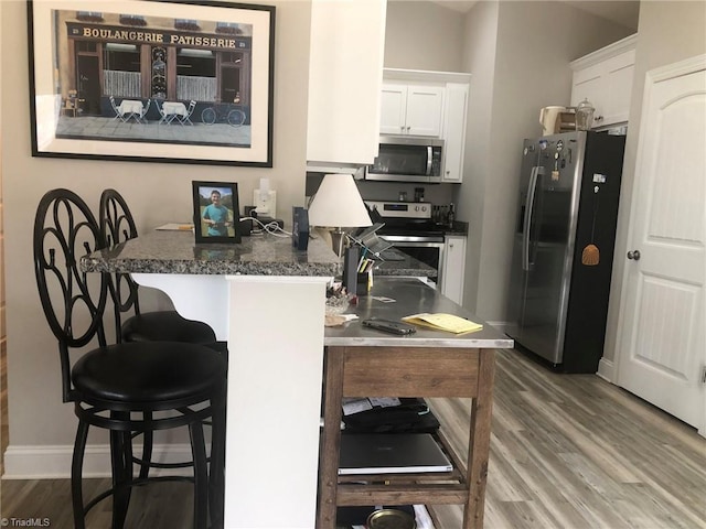 kitchen with dark countertops, white cabinetry, appliances with stainless steel finishes, and wood finished floors