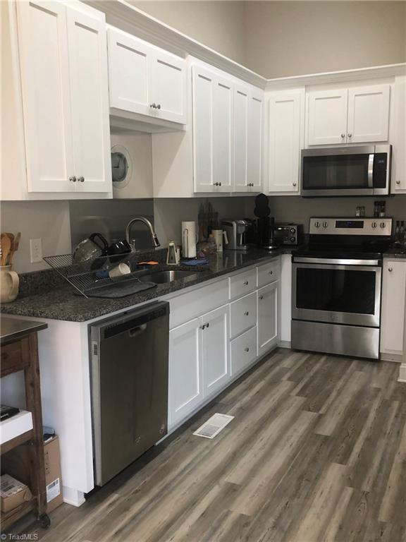 kitchen with dark wood finished floors, stainless steel appliances, visible vents, white cabinetry, and a sink