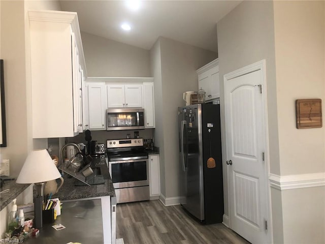 kitchen featuring appliances with stainless steel finishes, white cabinetry, a sink, wood finished floors, and dark stone counters