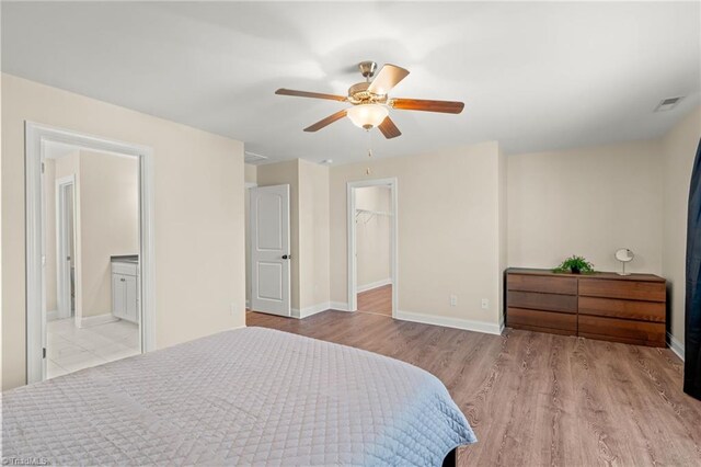 bedroom featuring ceiling fan, a spacious closet, connected bathroom, light wood-type flooring, and a closet