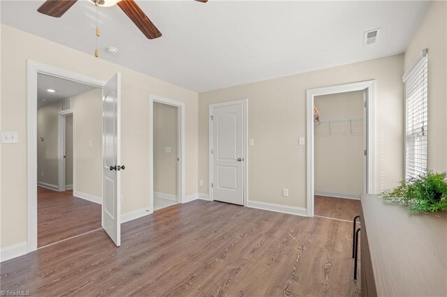 unfurnished bedroom with a walk in closet, a closet, wood-type flooring, and ceiling fan