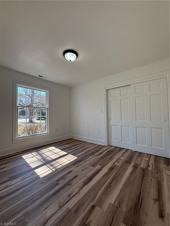 unfurnished bedroom with a closet, visible vents, baseboards, and wood finished floors