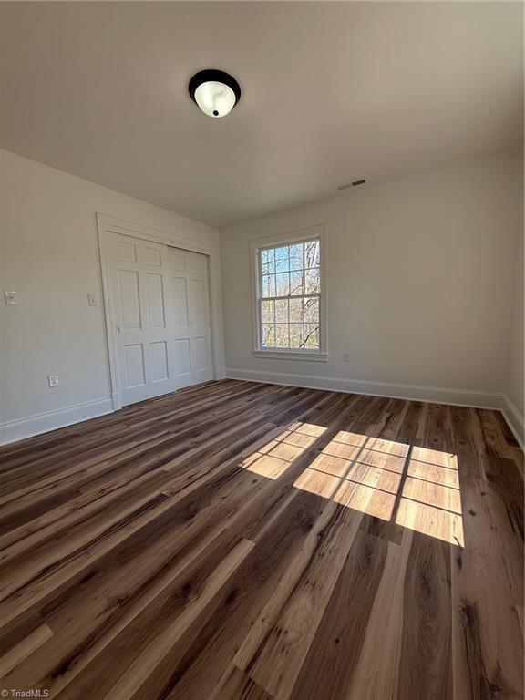 unfurnished bedroom with dark wood-style floors, a closet, visible vents, and baseboards