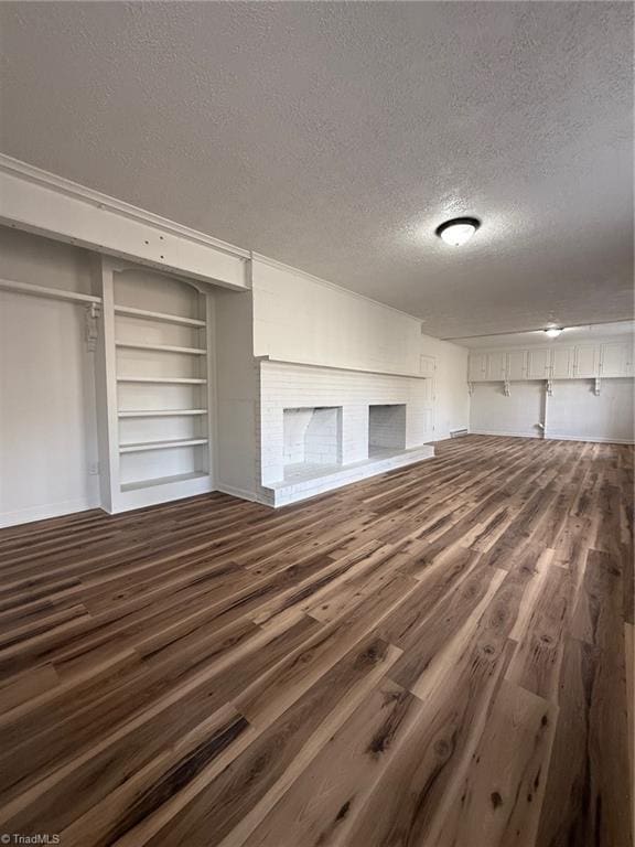 unfurnished living room featuring a brick fireplace, a textured ceiling, and wood finished floors