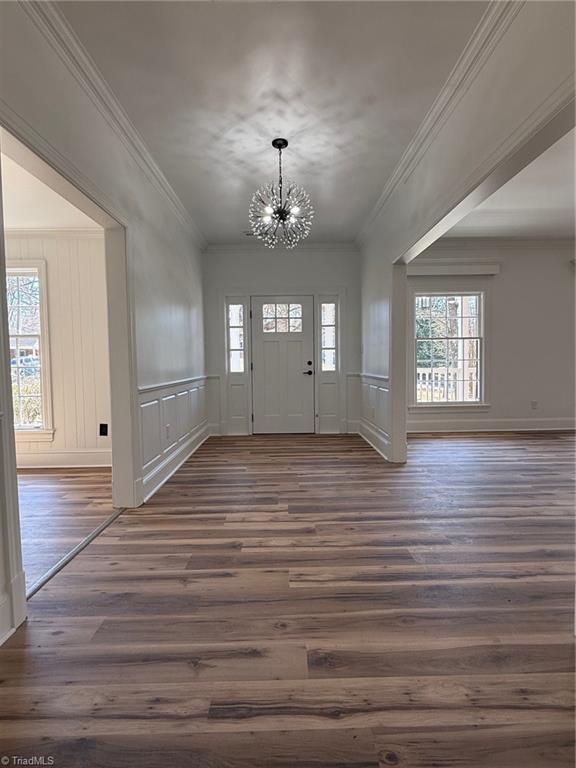 foyer featuring wainscoting, dark wood-type flooring, crown molding, a chandelier, and a decorative wall