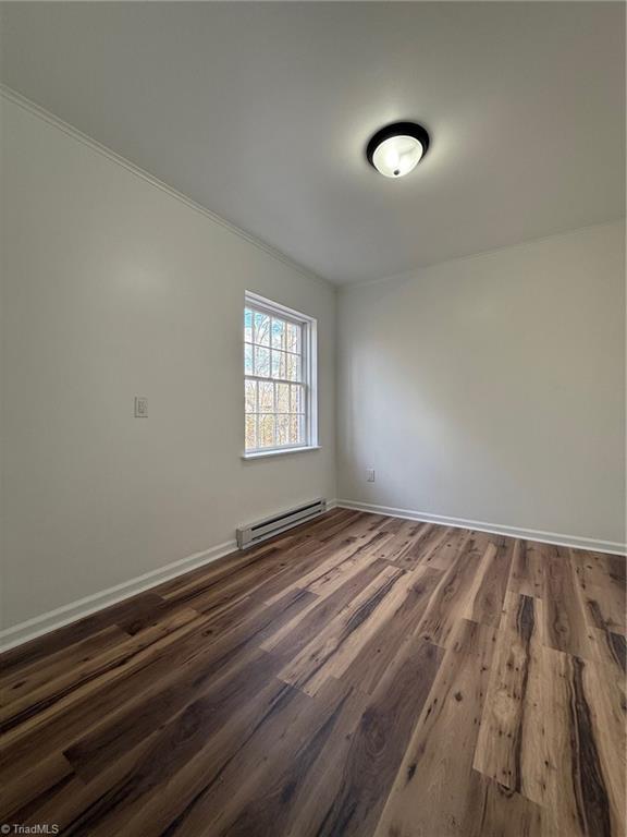 spare room with baseboards, a baseboard heating unit, and wood finished floors