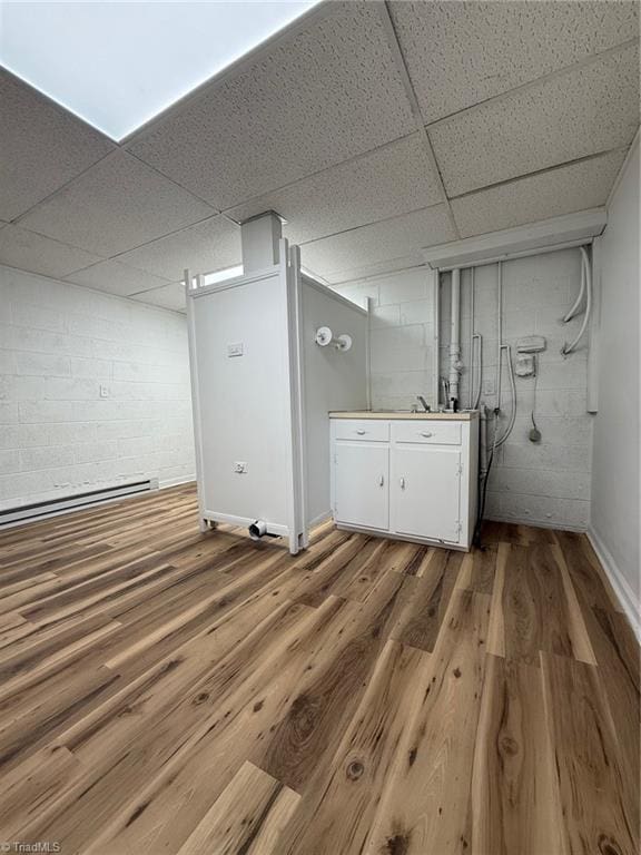 finished below grade area featuring a paneled ceiling, a baseboard radiator, wood finished floors, and concrete block wall