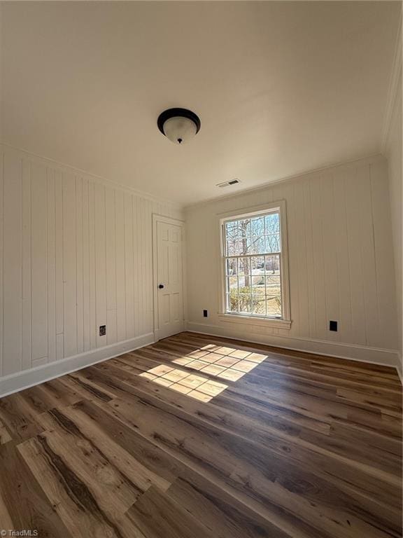 empty room with visible vents, crown molding, baseboards, and wood finished floors