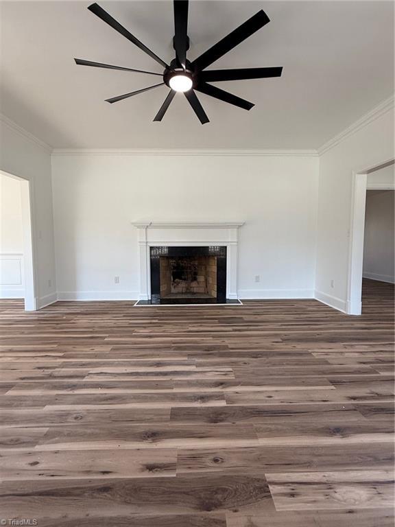 unfurnished living room featuring baseboards, a fireplace with flush hearth, ornamental molding, and wood finished floors