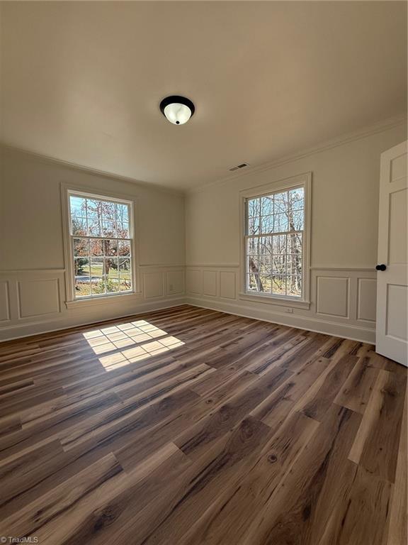 empty room featuring a wainscoted wall, crown molding, visible vents, and wood finished floors