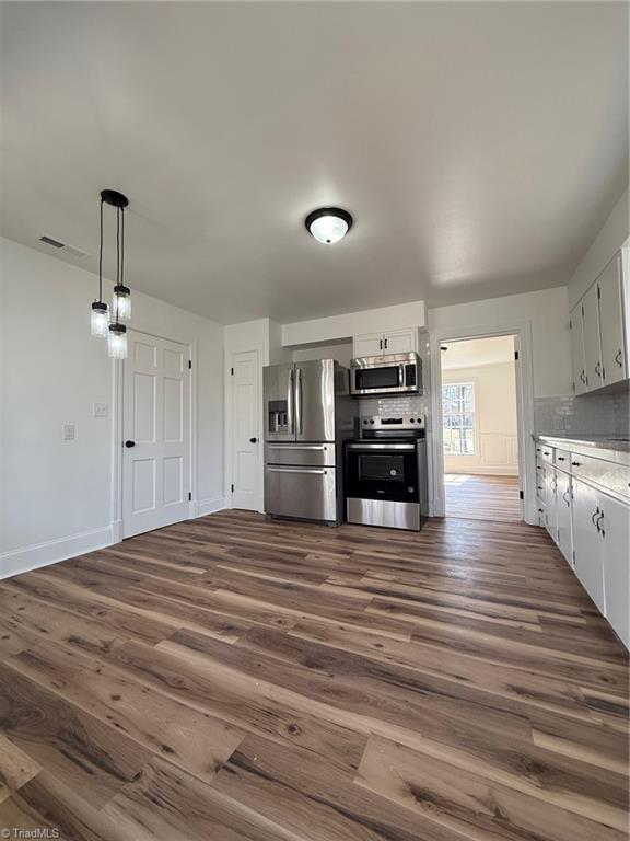 kitchen featuring appliances with stainless steel finishes, white cabinets, dark wood-type flooring, and decorative backsplash