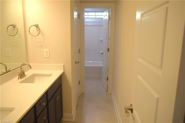 bathroom featuring a tub, tile patterned flooring, a sink, double vanity, and baseboards
