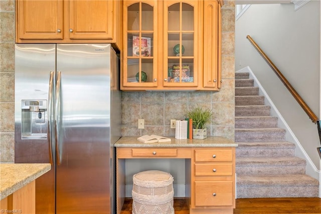 kitchen with light stone counters, backsplash, glass insert cabinets, and stainless steel fridge with ice dispenser