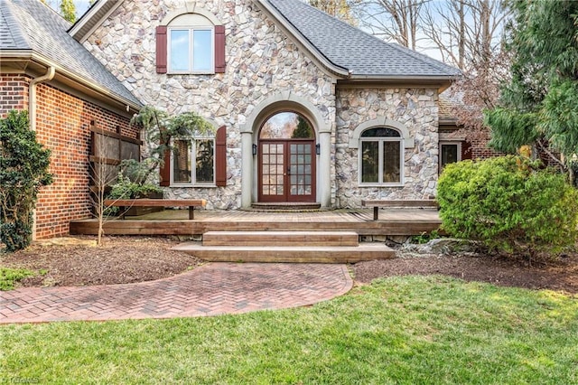 doorway to property with french doors, stone siding, and roof with shingles