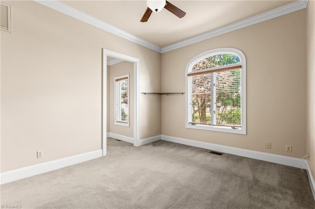 carpeted empty room with crown molding, visible vents, baseboards, and ceiling fan