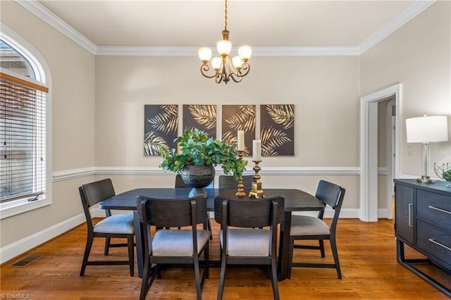 dining area featuring visible vents, crown molding, baseboards, wood finished floors, and a notable chandelier