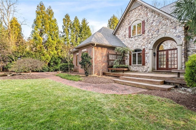 back of house with roof with shingles, a yard, french doors, stone siding, and brick siding