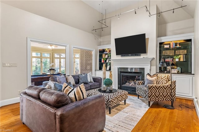 living area featuring a glass covered fireplace, track lighting, a high ceiling, and wood finished floors