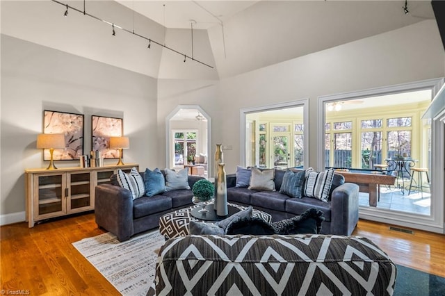 living room with visible vents, high vaulted ceiling, wood finished floors, arched walkways, and baseboards