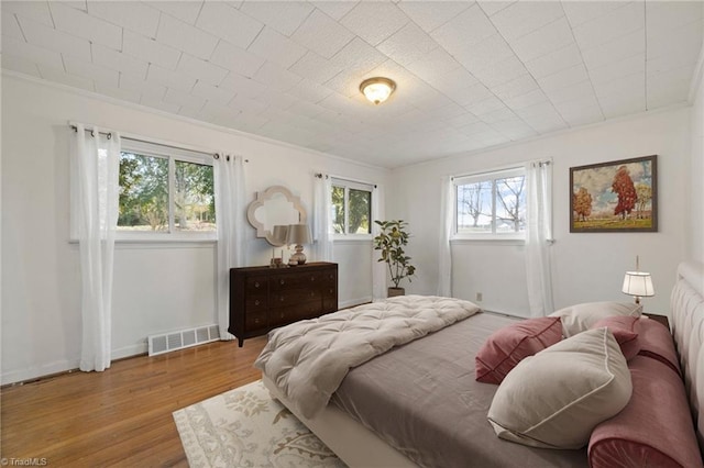 bedroom with ornamental molding, wood finished floors, visible vents, and baseboards