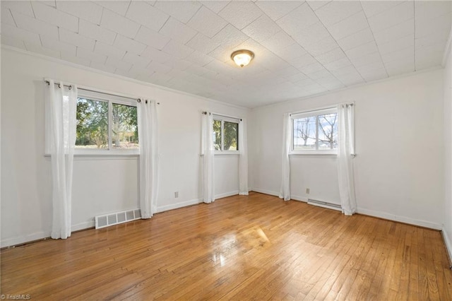 spare room with a baseboard heating unit, visible vents, baseboards, light wood finished floors, and crown molding