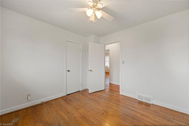 empty room featuring a ceiling fan, baseboards, visible vents, and wood finished floors