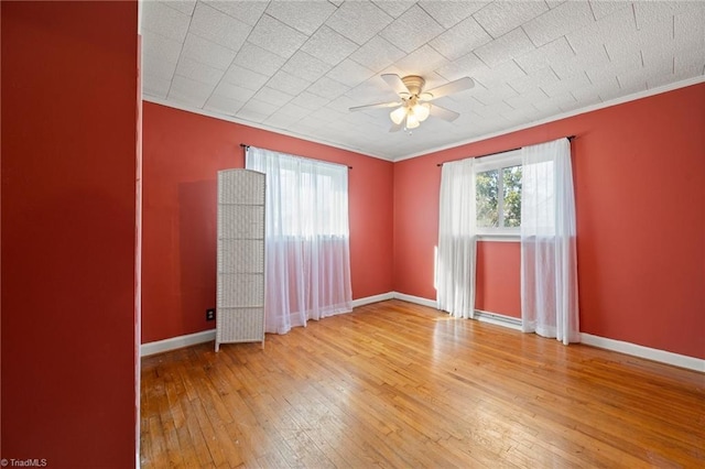 empty room featuring crown molding, a ceiling fan, hardwood / wood-style flooring, and baseboards