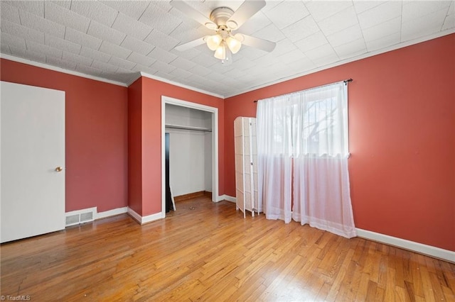 unfurnished bedroom featuring visible vents, baseboards, a closet, wood-type flooring, and crown molding