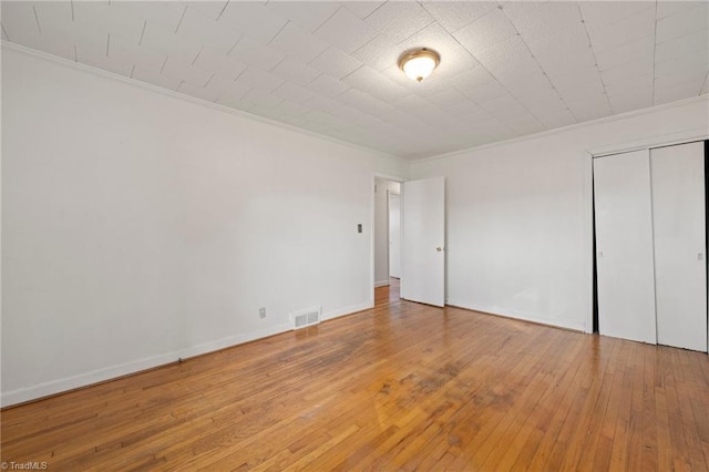 unfurnished bedroom featuring hardwood / wood-style flooring, visible vents, baseboards, a closet, and crown molding