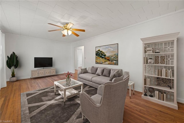 living room featuring a ceiling fan, ornamental molding, baseboards, and wood finished floors