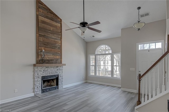 unfurnished living room featuring ceiling fan, a wealth of natural light, light hardwood / wood-style flooring, and a fireplace