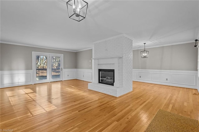 unfurnished living room with light wood-type flooring, an inviting chandelier, a brick fireplace, and crown molding