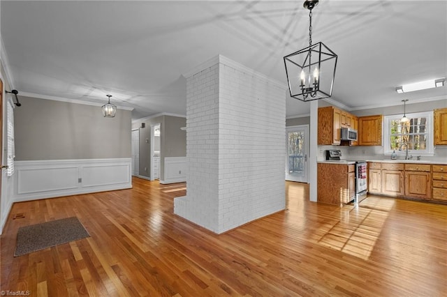 kitchen featuring hanging light fixtures, ornamental molding, light wood-type flooring, and appliances with stainless steel finishes