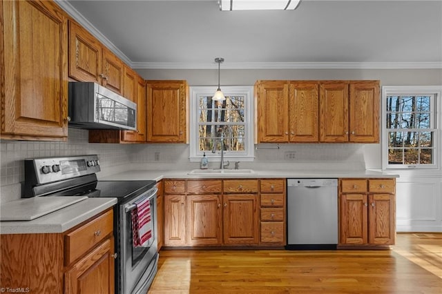 kitchen with sink, stainless steel appliances, pendant lighting, light wood-type flooring, and ornamental molding