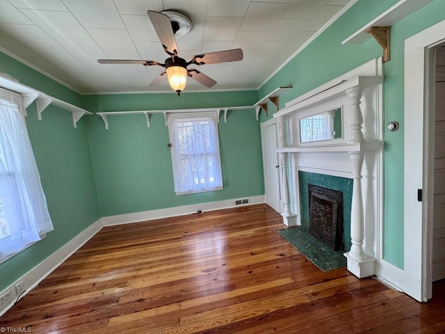 unfurnished living room featuring dark wood-type flooring, ceiling fan, ornamental molding, and a fireplace