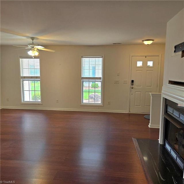 unfurnished living room featuring dark wood-style flooring, ceiling fan, baseboards, and a fireplace with flush hearth