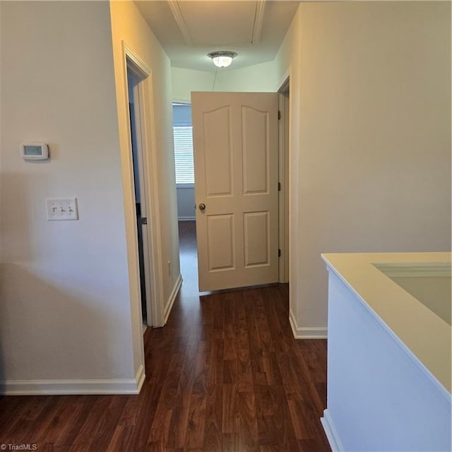 hallway featuring attic access, baseboards, and dark wood-style floors