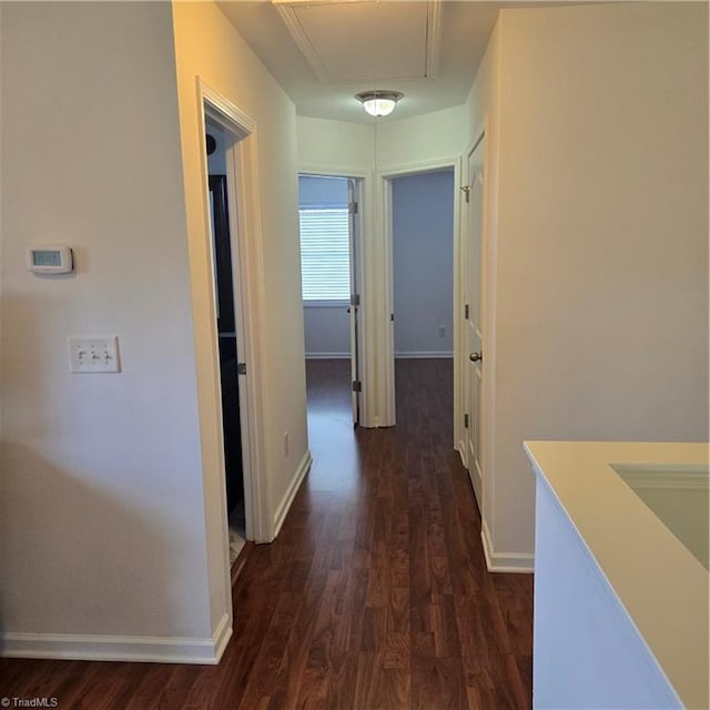 hall with attic access, dark wood-type flooring, and baseboards
