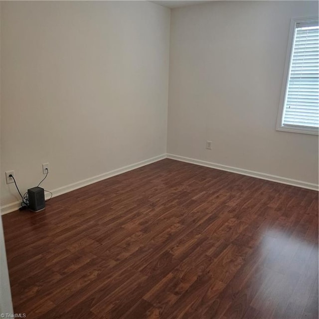 spare room with baseboards and dark wood-style floors