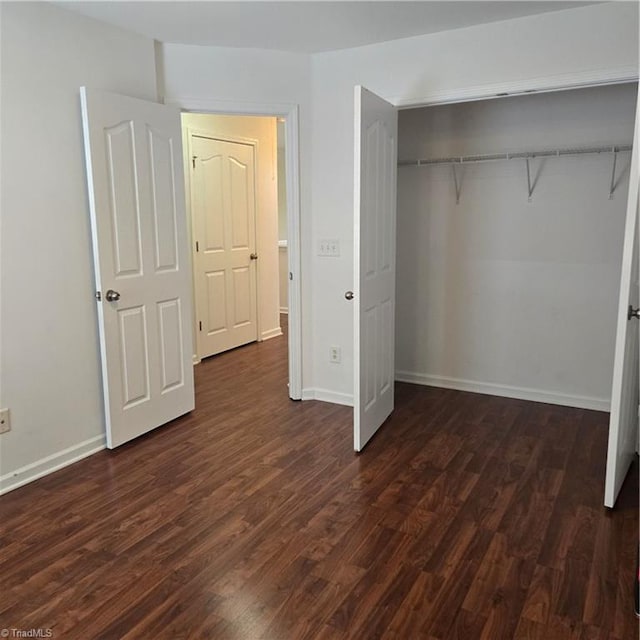 unfurnished bedroom featuring a closet, dark wood-style flooring, and baseboards