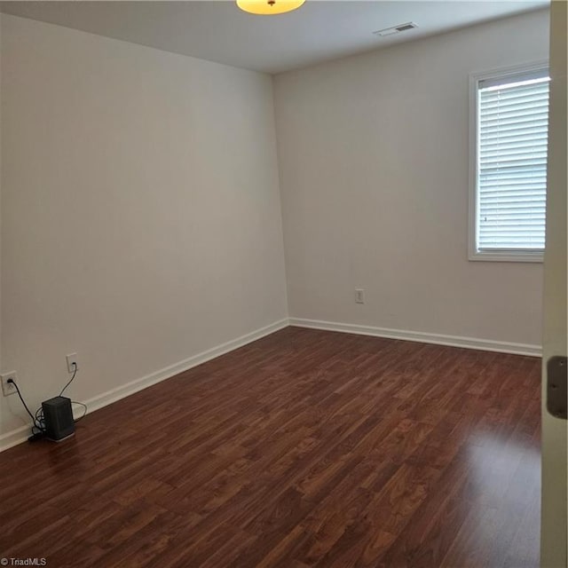 empty room with baseboards, dark wood-type flooring, and visible vents