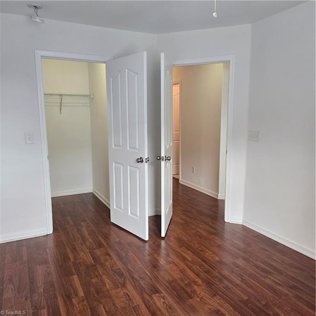 unfurnished bedroom featuring a walk in closet, baseboards, dark wood-type flooring, and a closet