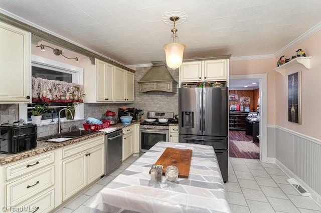 kitchen with pendant lighting, premium range hood, sink, cream cabinetry, and stainless steel appliances