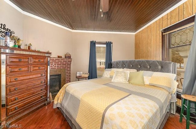 bedroom with dark wood-type flooring, a brick fireplace, wooden walls, wood ceiling, and ornamental molding