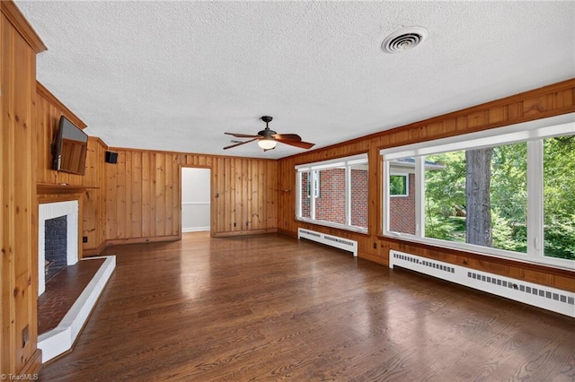 503 Tarleton Ave, Burlington, NC 27215 - unfurnished living room featuring a textured ceiling, baseboard heating, ceiling fan, dark wood-style floors, and wooden walls