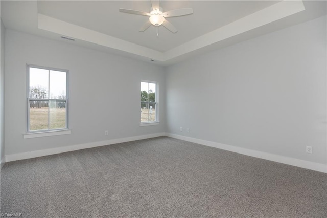 unfurnished room with carpet flooring, a raised ceiling, baseboards, visible vents, and ceiling fan